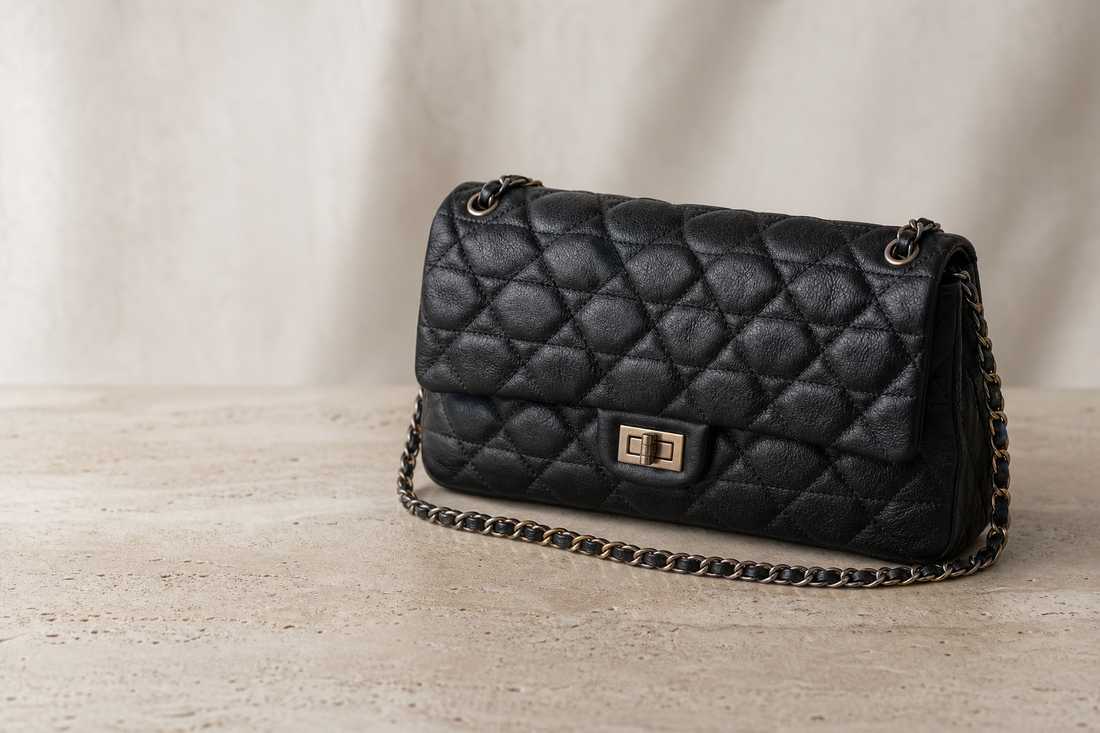Editorial still life of an unbranded black quilted leather chain shoulder bag on a neutral stone surface