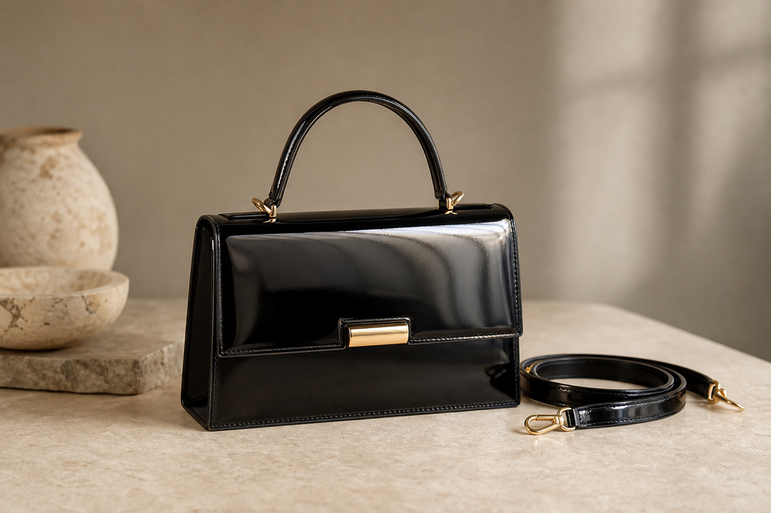Editorial still life of an unbranded black patent-leather compact top-handle bag with a detachable shoulder strap.
