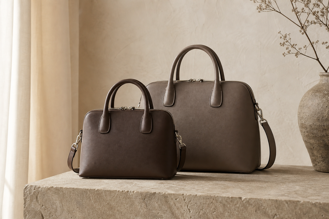 Two unbranded structured leather handbags in compact and medium sizes on a warm stone pedestal, illustrating a pre-owned size comparison.