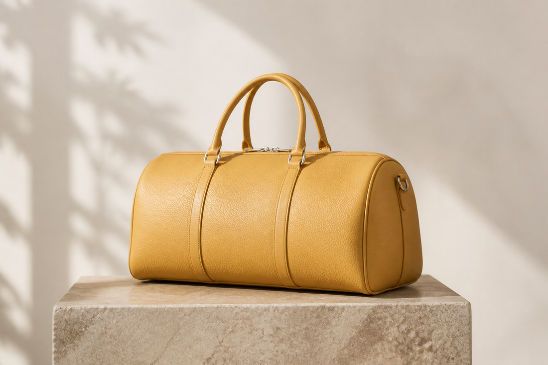 Unbranded honey-yellow leather travel handbag with rounded ends and double top handles on a stone pedestal, illustrating a pre-owned Victoria-style bag buying guide.