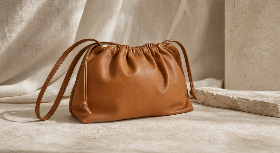 Editorial still life of an unbranded soft caramel leather drawstring bag on warm neutral stone for a pre-owned Loewe Flamenco buying guide
